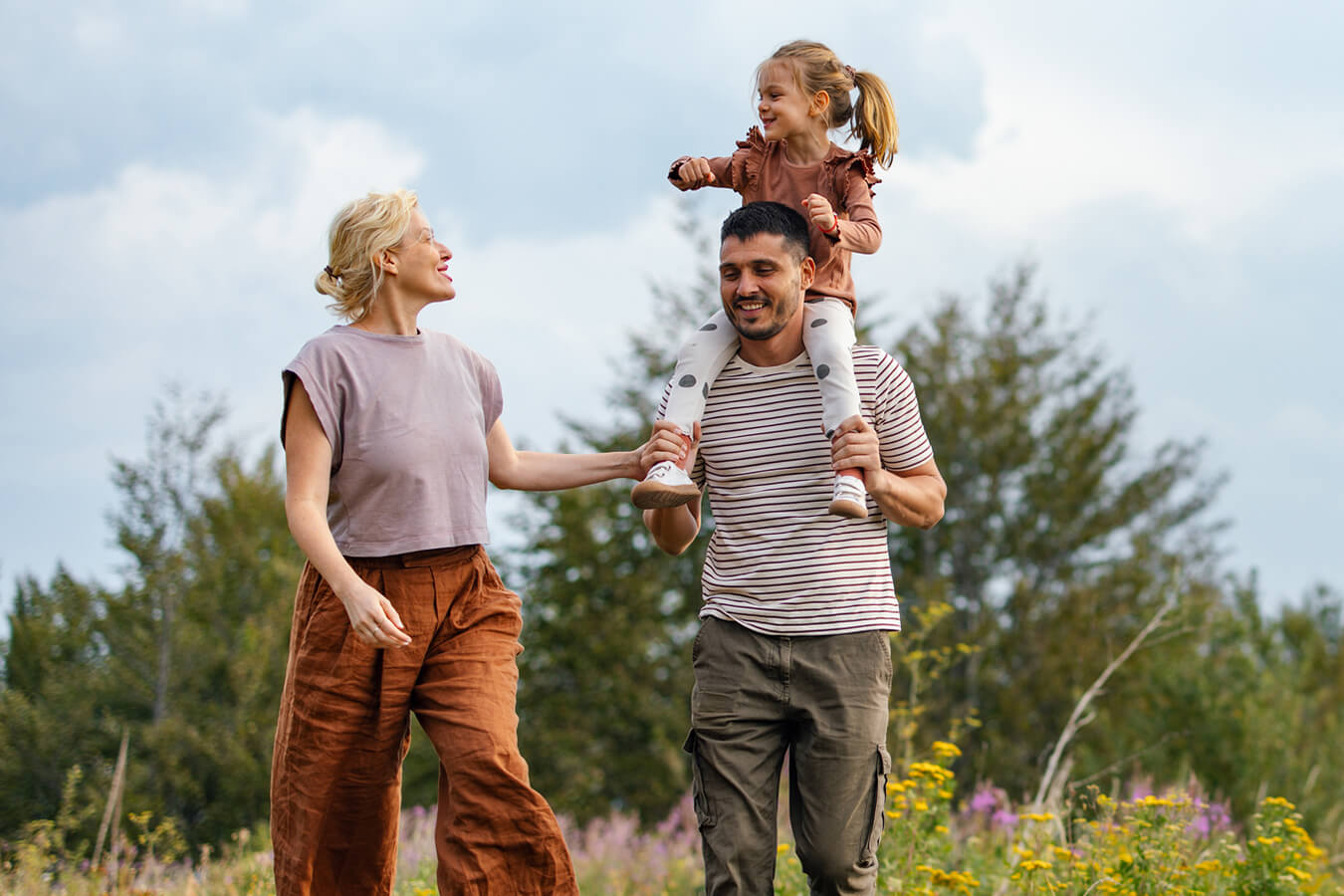 A happy family of three walking through a field of wildflowers.