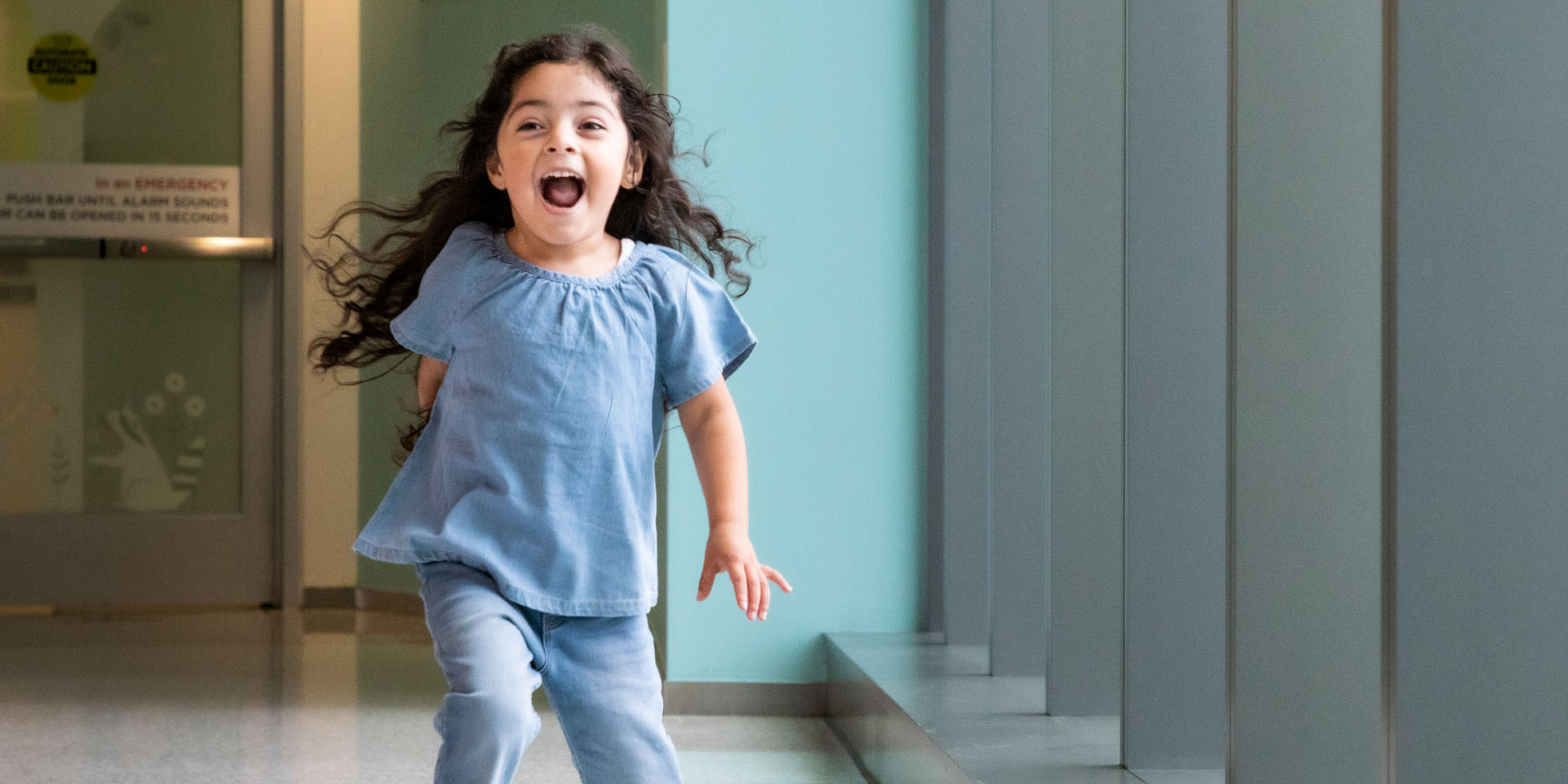 Young girl in blue runs down a hall laughing