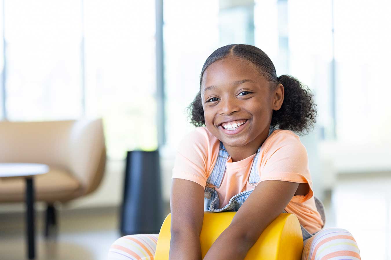 Girl in peach t-shirt and overalls smiles at camera