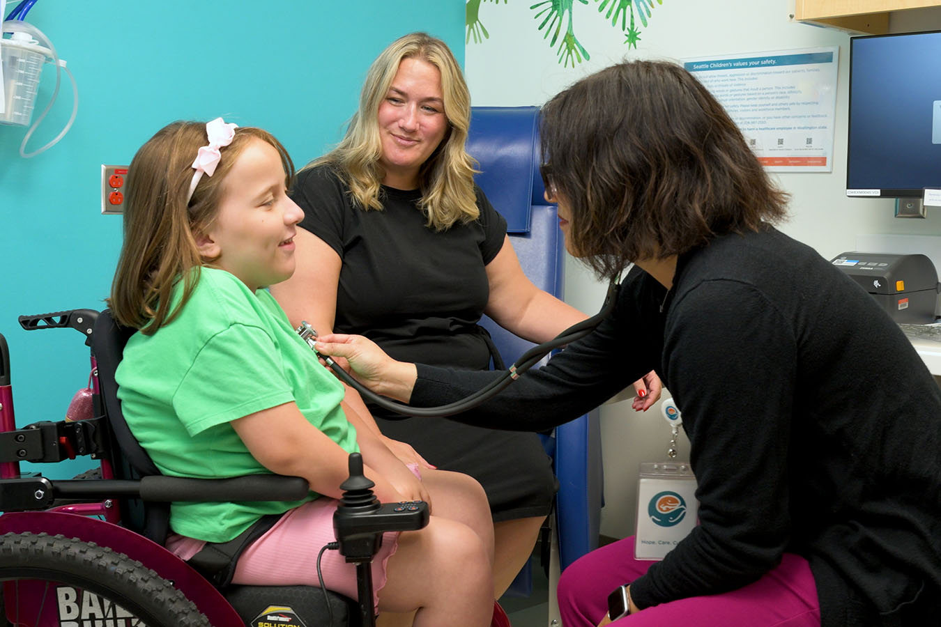 A doctor checks a child's heart with a stethoscope while a mother looks on