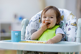 a toddler smiling and sticking something in their mouth while sitting in a highchair