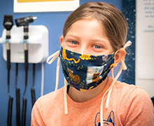 Smiling girl wearing a mask while sitting in a medical exam room