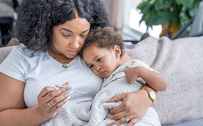 A mother holds her toddler while checking a thermometer