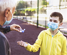 Man squeezes hand sanitizer into a teen boy's hand