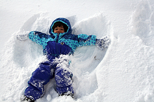 A child in a blue snowsuit laying in the snow making a snow angel