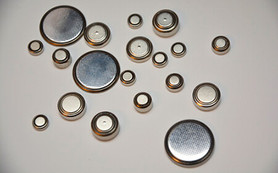 A cluster of small and large circular silver button batteries, commonly found in small electronics, resting on a white surface.