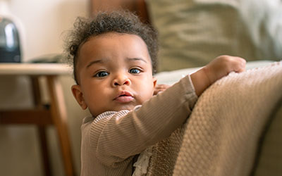 A toddler stands up against a couch