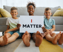 Children sitting in front of a couch. The middle child holds a sign that says "I Matter".