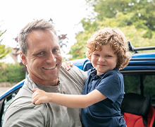 A father holds his son in front of a car