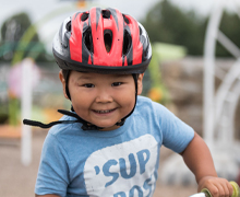 A little boy wears a helmet on his bike