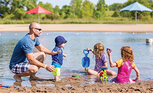 A man supervises three young children on a beach.