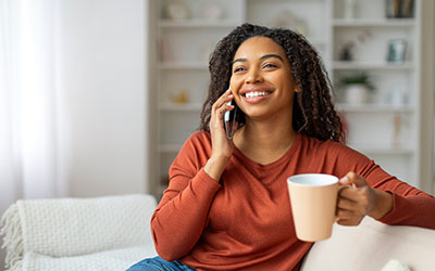 Parent smiling while on the phone and holding a coffee mug.