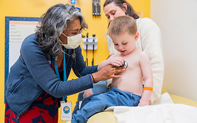 Doctor using a stethoscope on a young child with parent nearby.