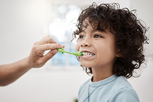 An adult brushes a child's teeth.