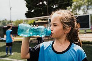 A girl in a sports jersey drinks from a water bottle.