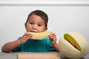 A young boy eats a slice of melon