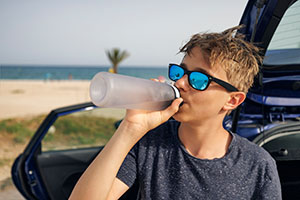 A teen boy drinks from a water bottle in front of a car