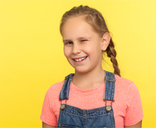 A girl in overalls exhibiting a tic