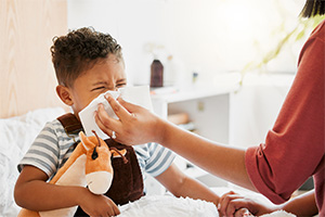 a mother putting a tissue to their child's nose so they blow it