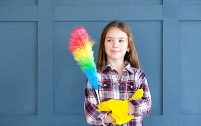 A girl with kitchen gloves holds a duster
