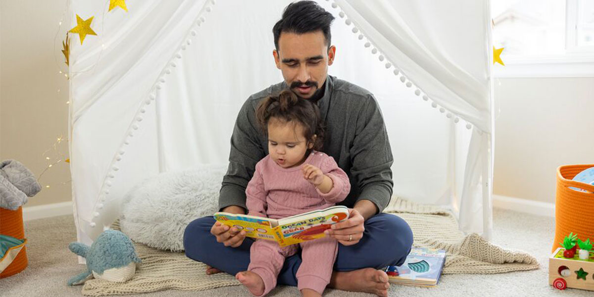 father sits on the floor reading to his daughter