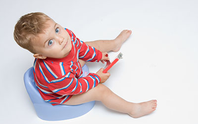 A toddler boy sits on a portable potty