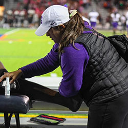 An athletic trainer works on an athlete's leg on the sideline of a playfield