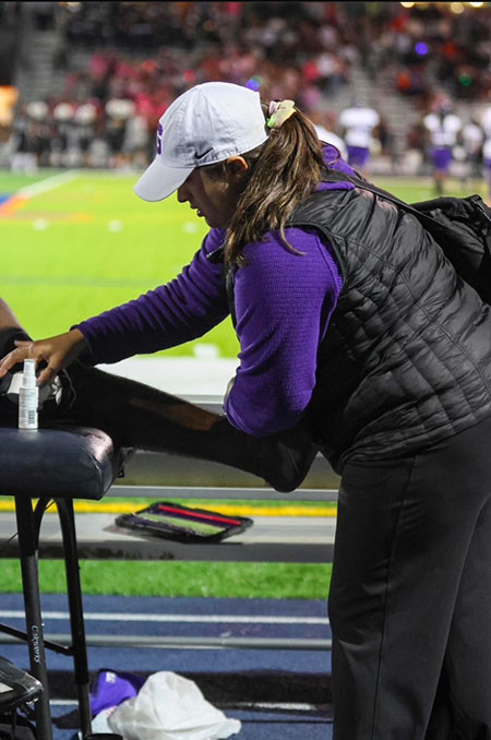An athletic trainer works on an athlete's leg on the sideline of a playfield