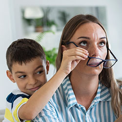 A mother looks frustrated as her kids play with her glasses and distract her from her work