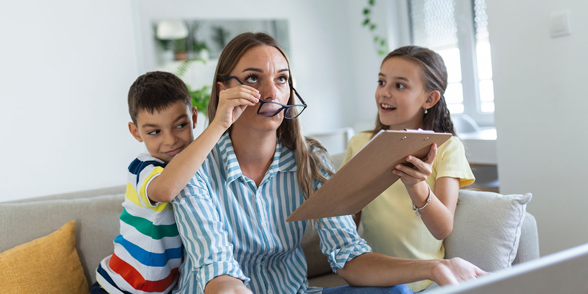 A mother looks frustrated as her kids play with her glasses and distract her from her work