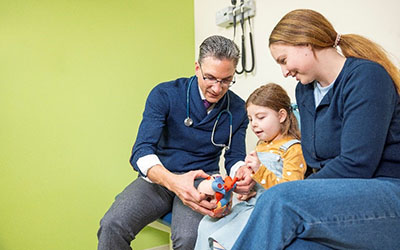 A Seattle Children's doctor shows a model heart to a young girl and her mother