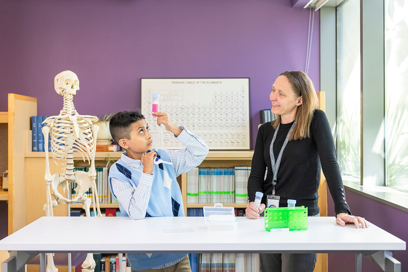 A boy looks at a test tube while a Seattle Children's doctor looks on