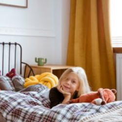 A blond school-aged girl lays on plaid comforter on her bed 