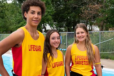 Three lifeguards stand in front of a pool.