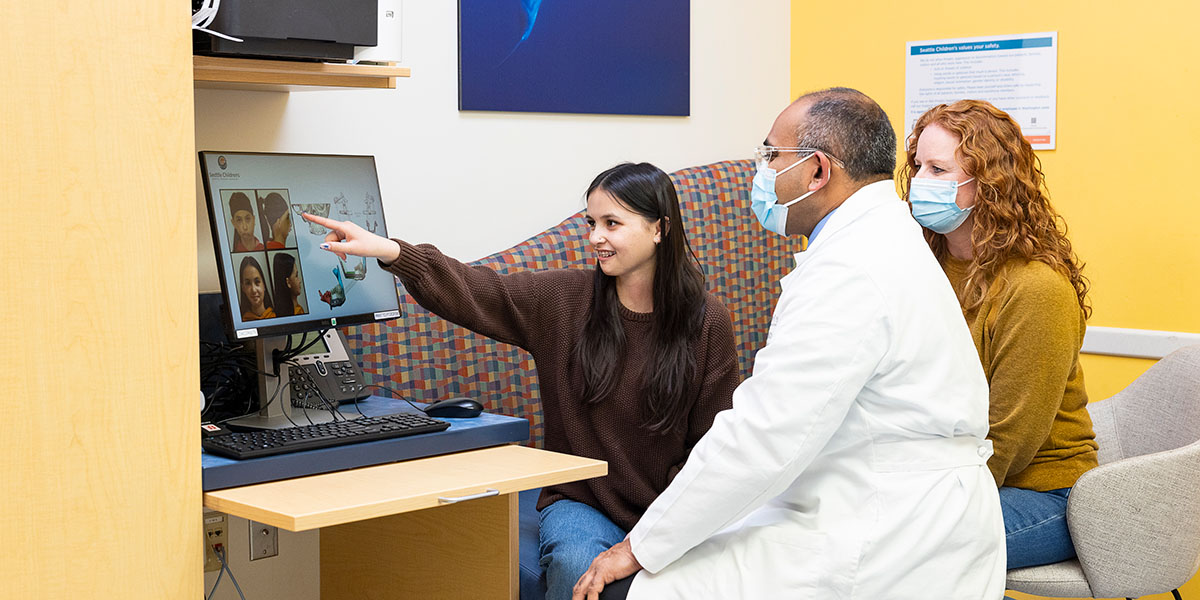 A teenaged patient points to a computer screen her doctor and mother are looking at