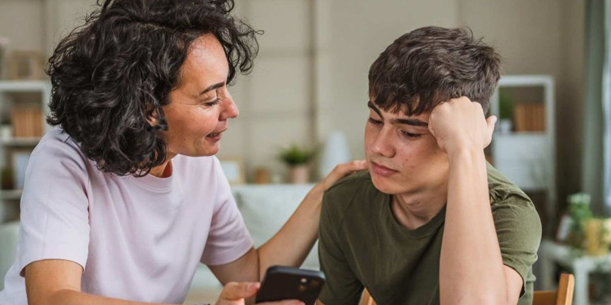 A mother and son talk while looking at a phone