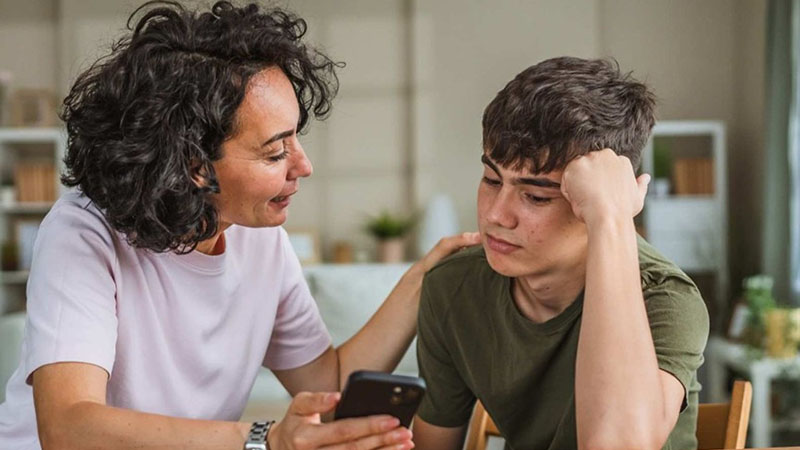 A mother and son talk while looking at a phone