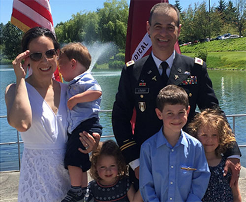 A family stands in front of a lake. The father is in a military uniform.