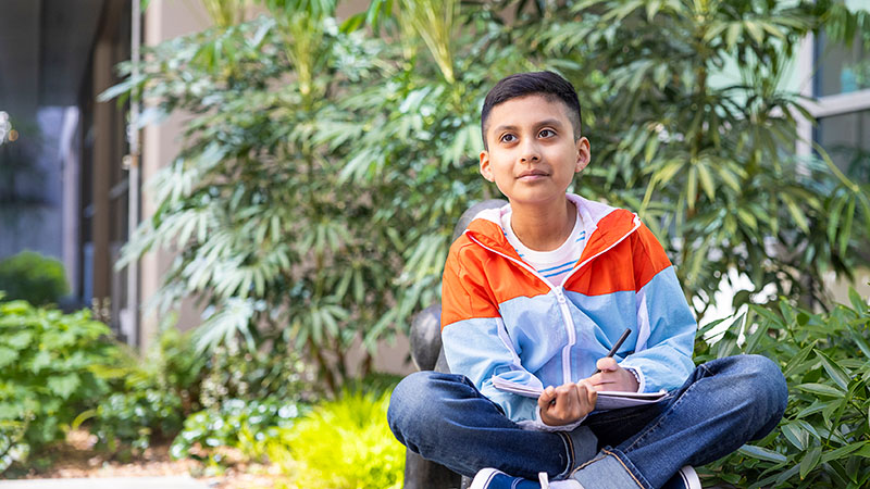 A boy holds a sketchbook and looks into the distance