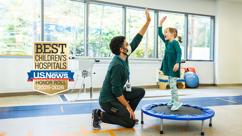 U.S. News & World Report Best Children's Hospitals Honor Roll badge, next to a photo of a therapist high-fiving a child on a trampoline.