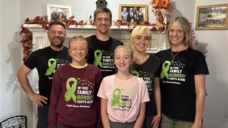 A family a six stands together in front of a fireplace, all wearing shirts that say, "In this family, nobody fights alone."
