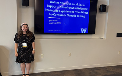 A woman stands in front of a presentation at a conference
