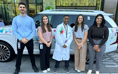 Rao lab researchers pose in front of a car