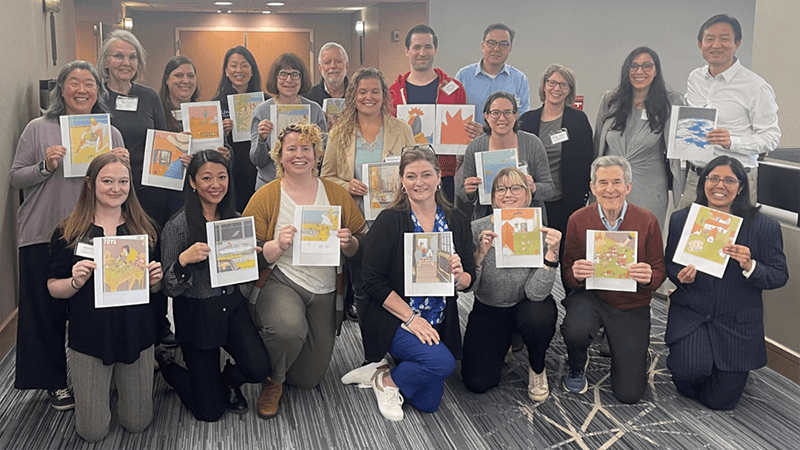 A group of diverse people standing and kneeling, each holding up a different piece of artwork.