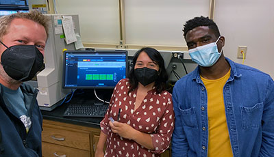Three researchers stand in front of data on a screen