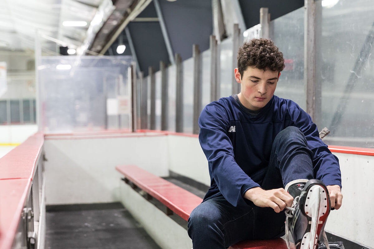 Adolescent boy sitting on a bench at a hockey rink tying on his skates