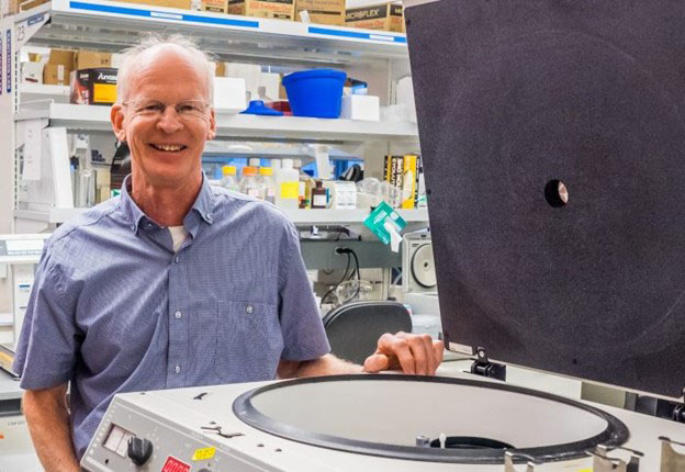 A researcher stands next to a machine used in gene editing.