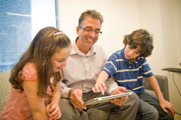 A man shows a boy and a girl something on a tablet computer