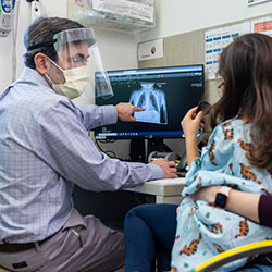 Dr. Cooper with a young girl and her mother in an exam room looking at a chest x-ray on a computer