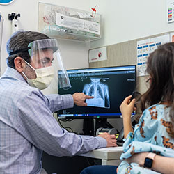 Seattle Children’s Dr.  Todd Cooper shows a young patient and her mother a lung X-ray on a computer screen in an exam room.